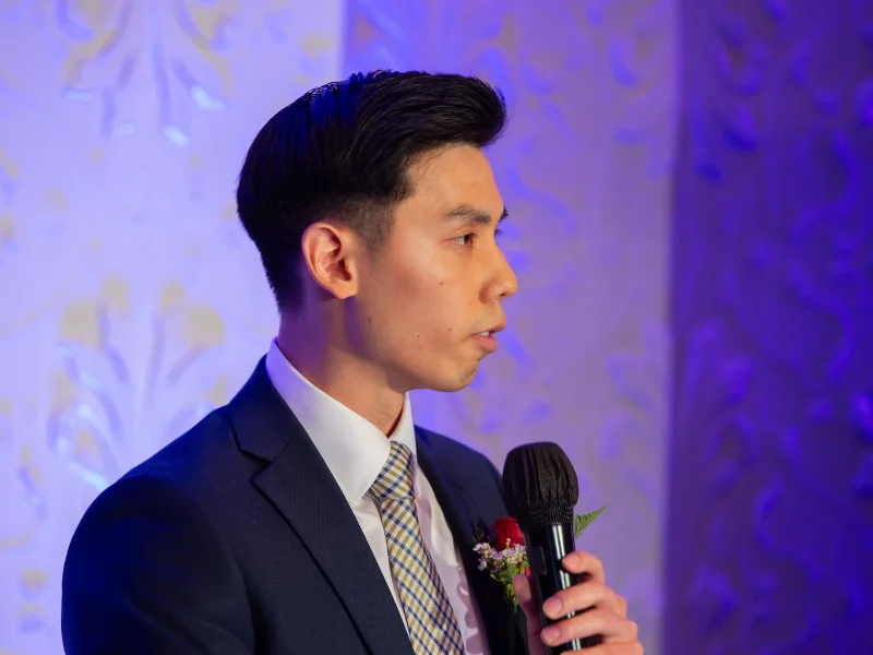 Treasurer Zachary Fu speaking at the podium as he accepts the honorary award for his father, Mr. Jason Fu.