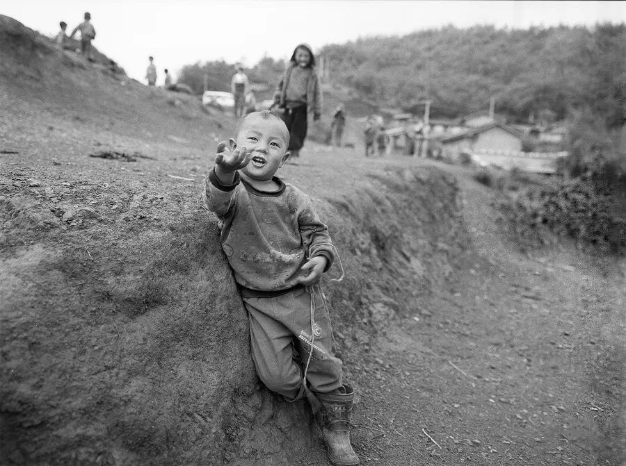 A boy waving from a dirt path, Liangshan Prefecture.